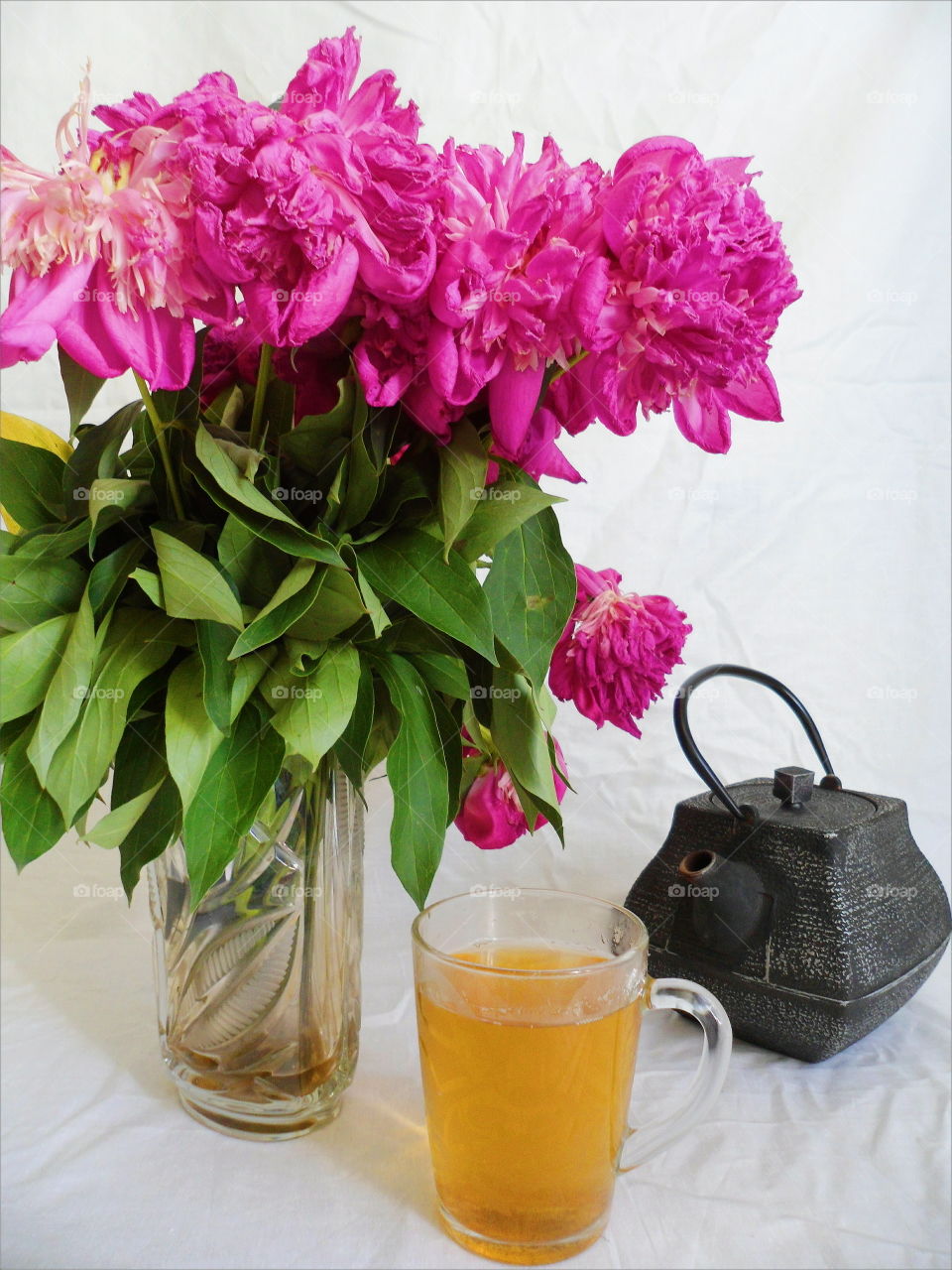 pink bouquet of wilted peony flowers, a cup of green tea and a tea pot