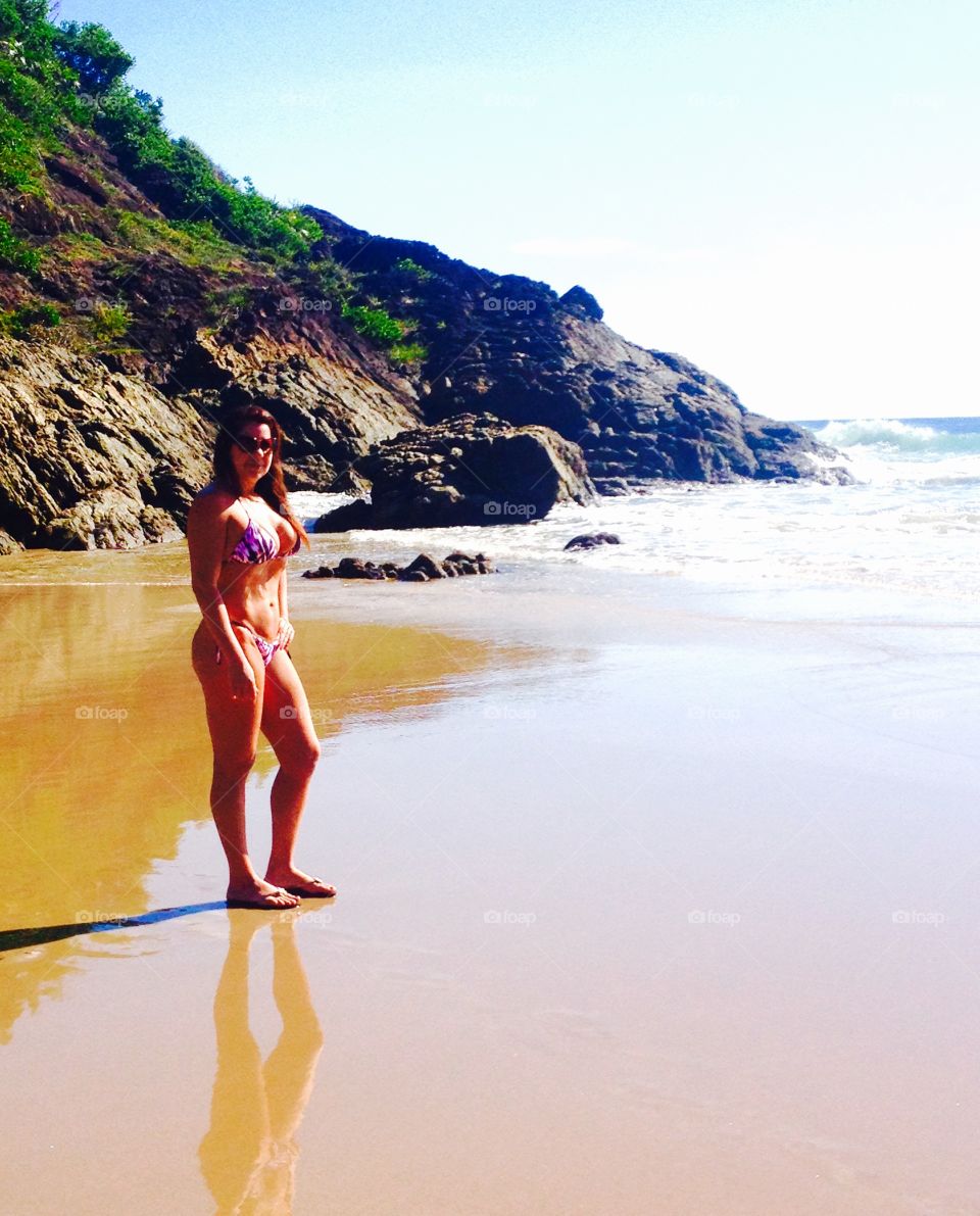 Young woman in bikini standing at beach near mountain