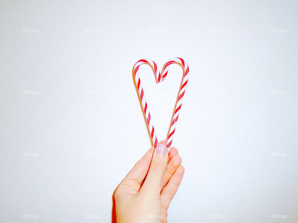 Hand holding a heart made of candy canes on white background