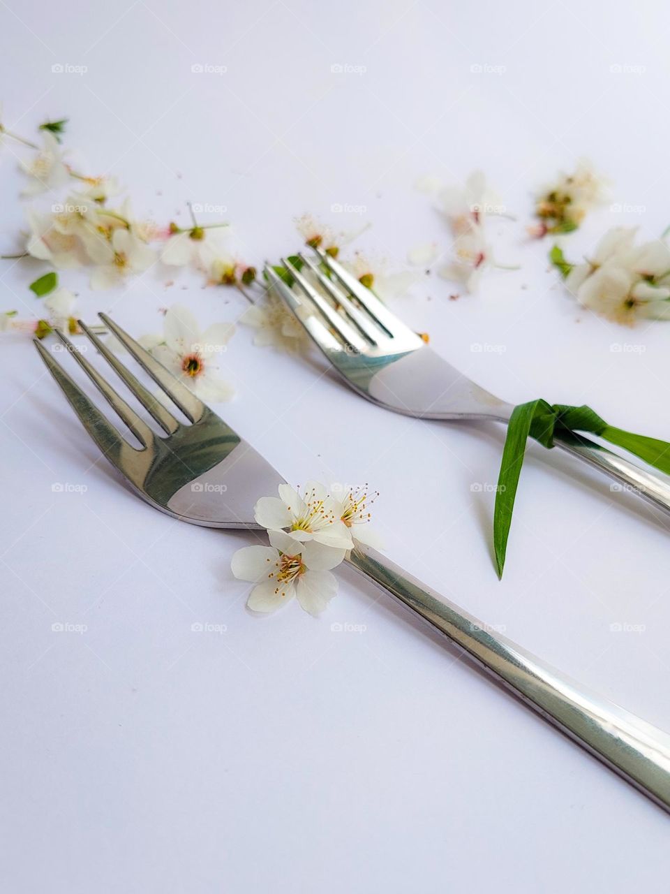 Two metal forks decorated with flowers and a grass tie, as a like a woman and a man,  on the white table decorated with flowers