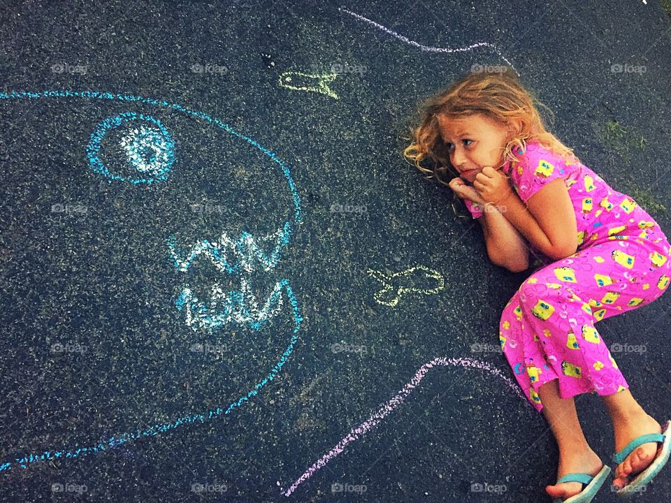 Scared girl lying on asphalt looking at drawing of shark
