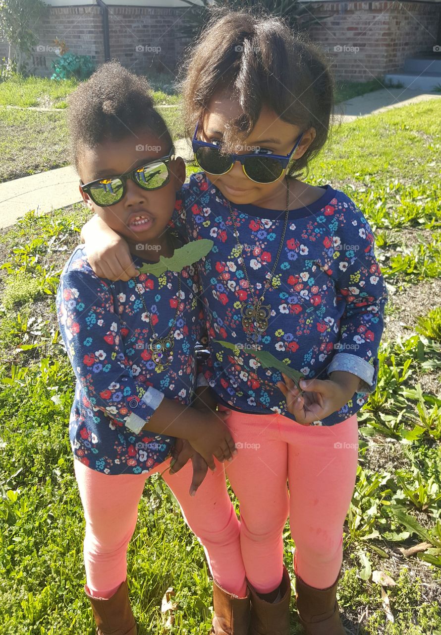 Two African girls wearing sunglasses standing on grass