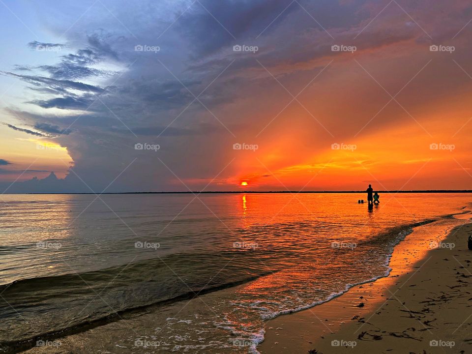 A couple look for sea shells during sunset. Sunsets bring with itself, such orangish colors in the sky which are beautiful to stare at. 