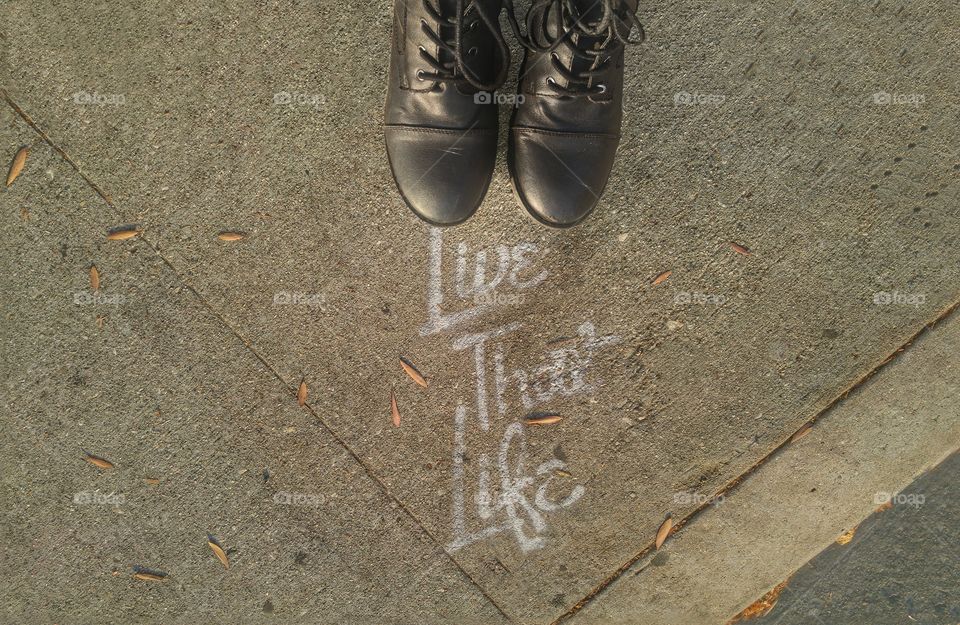 Black boots standing by the text "live that life" written on the pavement.