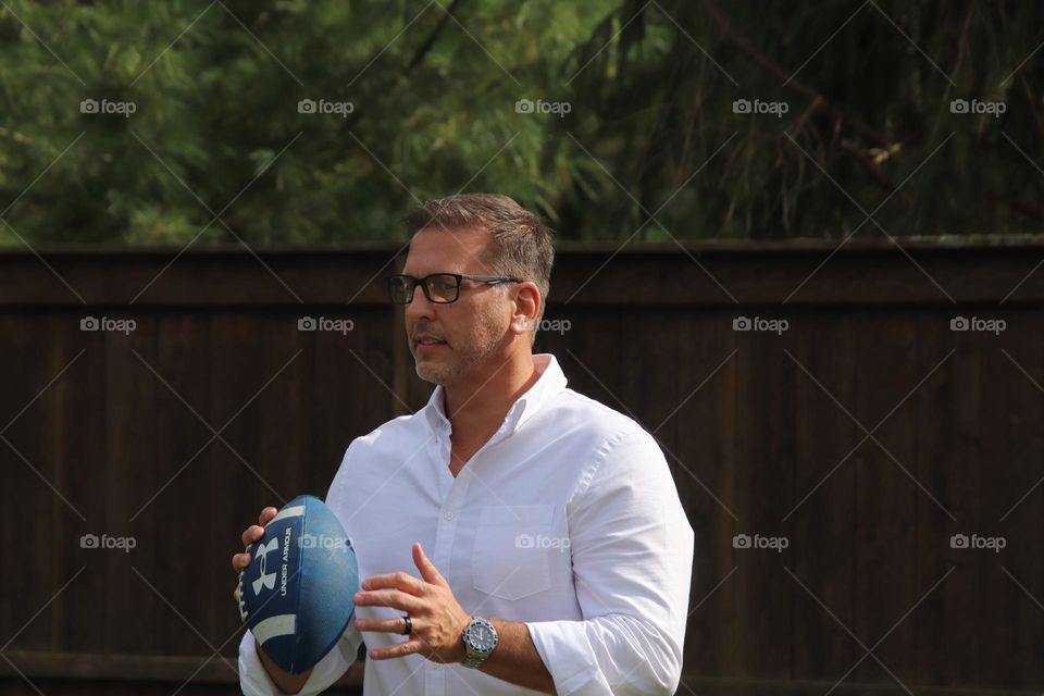 Man with short beard smiling outdoors on sunny day holding football