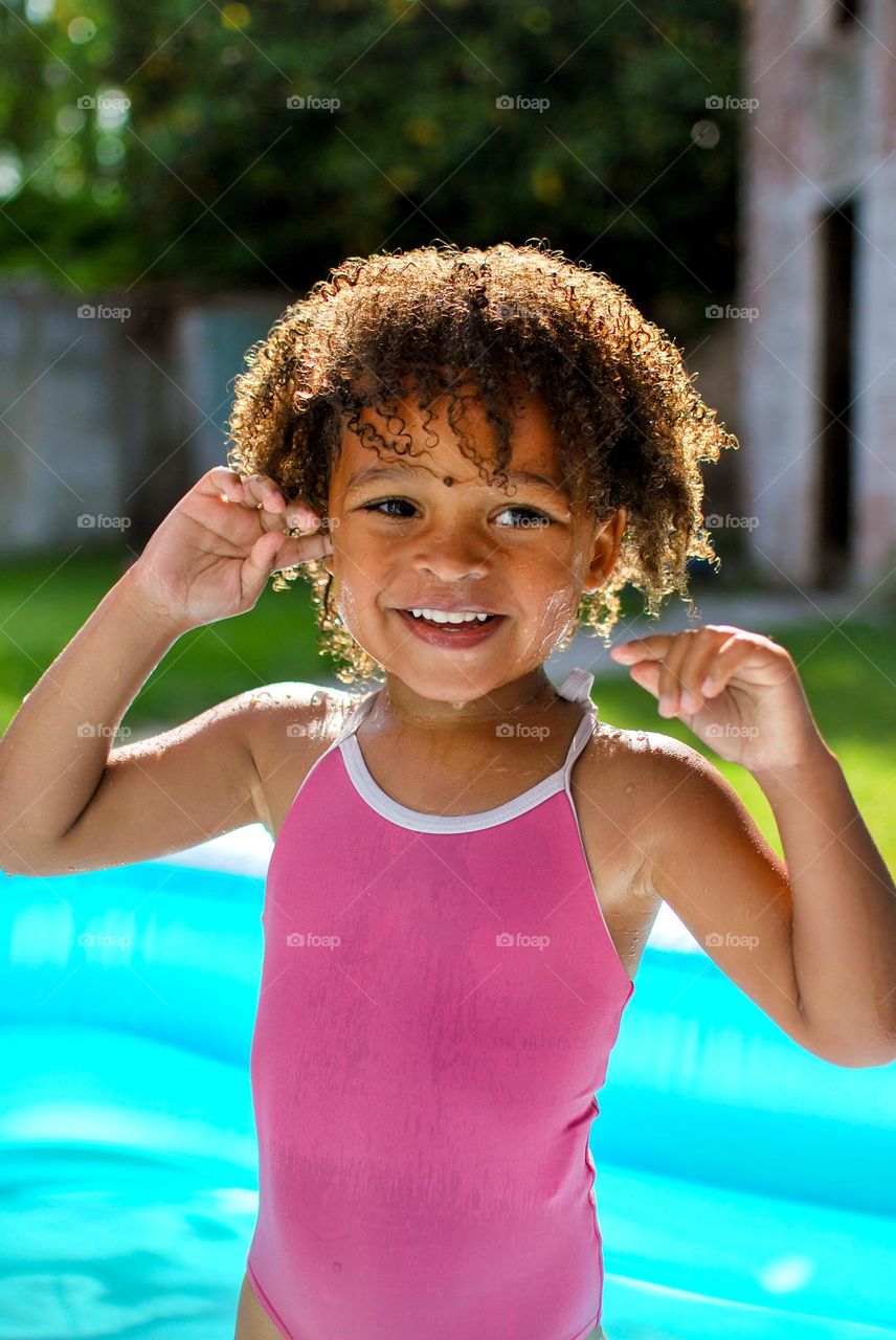 Cute little girl enjoying some playtime in a swimming pool during a hot summer day, looking for refreshment