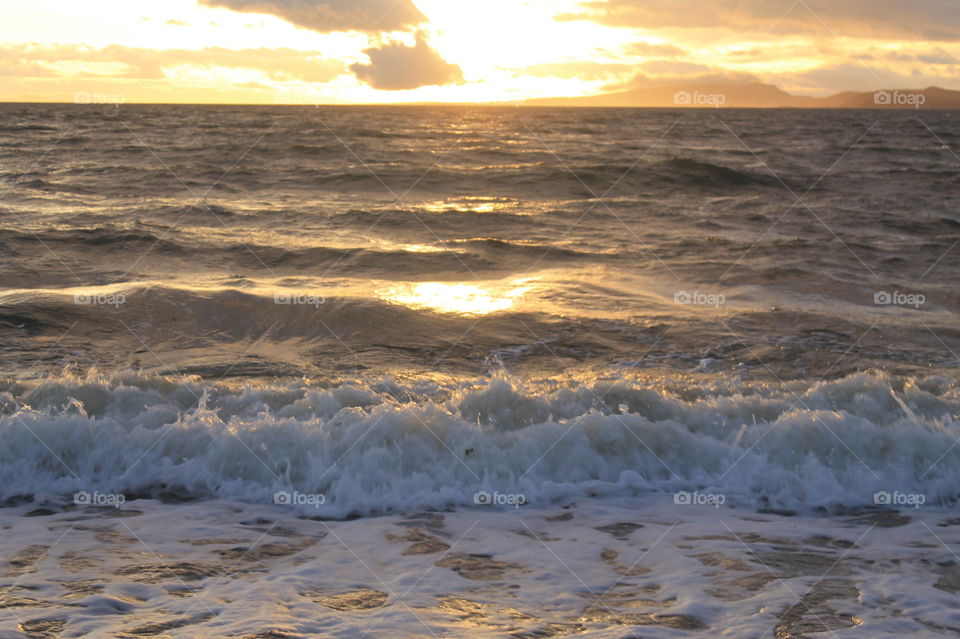 A sunrise shot of the ocean on a slightly windy Pacific Coast morning. The rising tide created frothy waves breaking on the shore. The sun shone through the clouds creating beautiful colour in the sky & sea & making the distant islands golden. 🌤