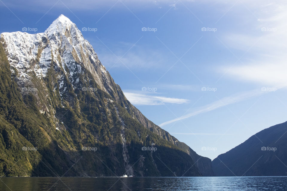 A boat cruises past a large mountain on Milford Sound, New Zealand