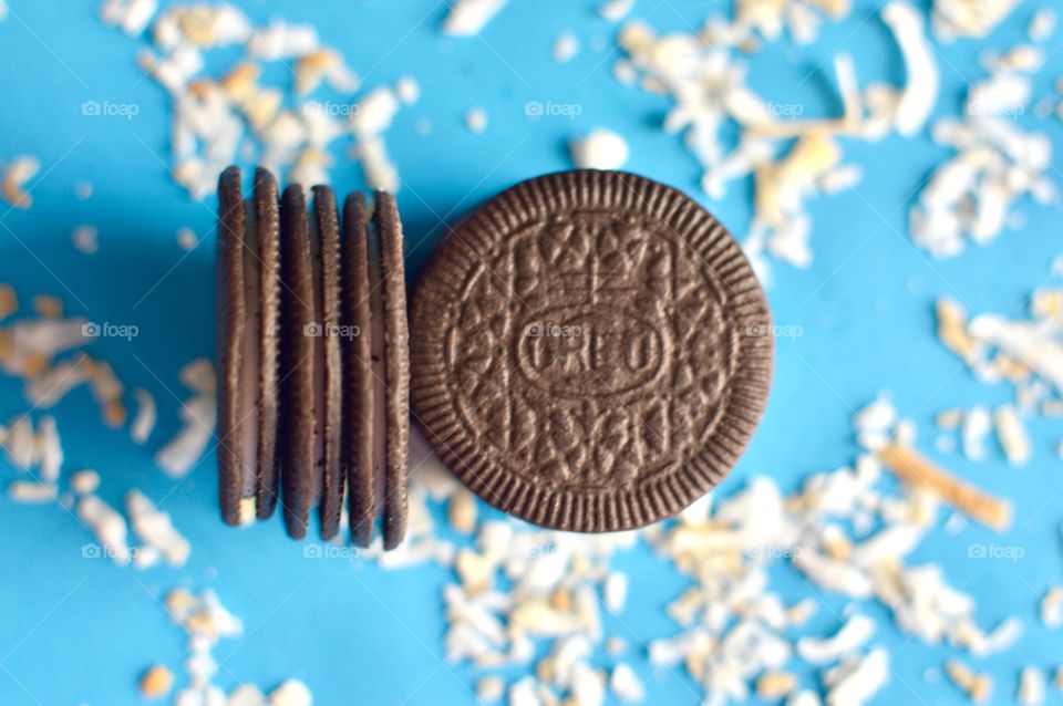 A stack of coconut Oreo thin cookies on a blue background with coconut shreds flat lay