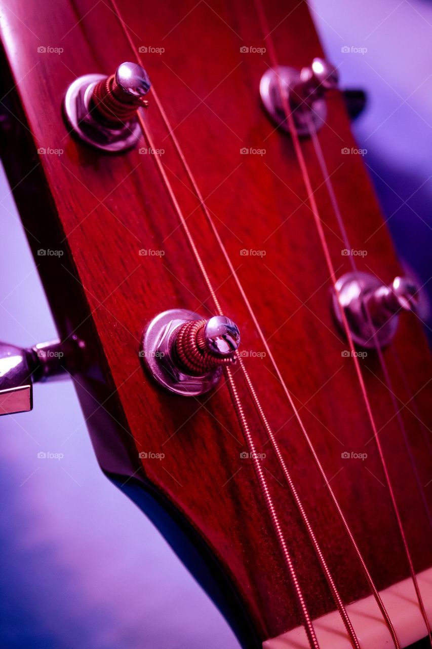 Let the music begin! A close up of a red wood acoustic guitar head with silver tuning knobs and steel strings.