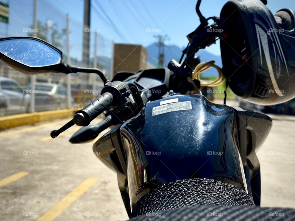 Black motorcycle parked in a parking lot with a helmet hanging on it, in a sunny day with a mountain in the background.