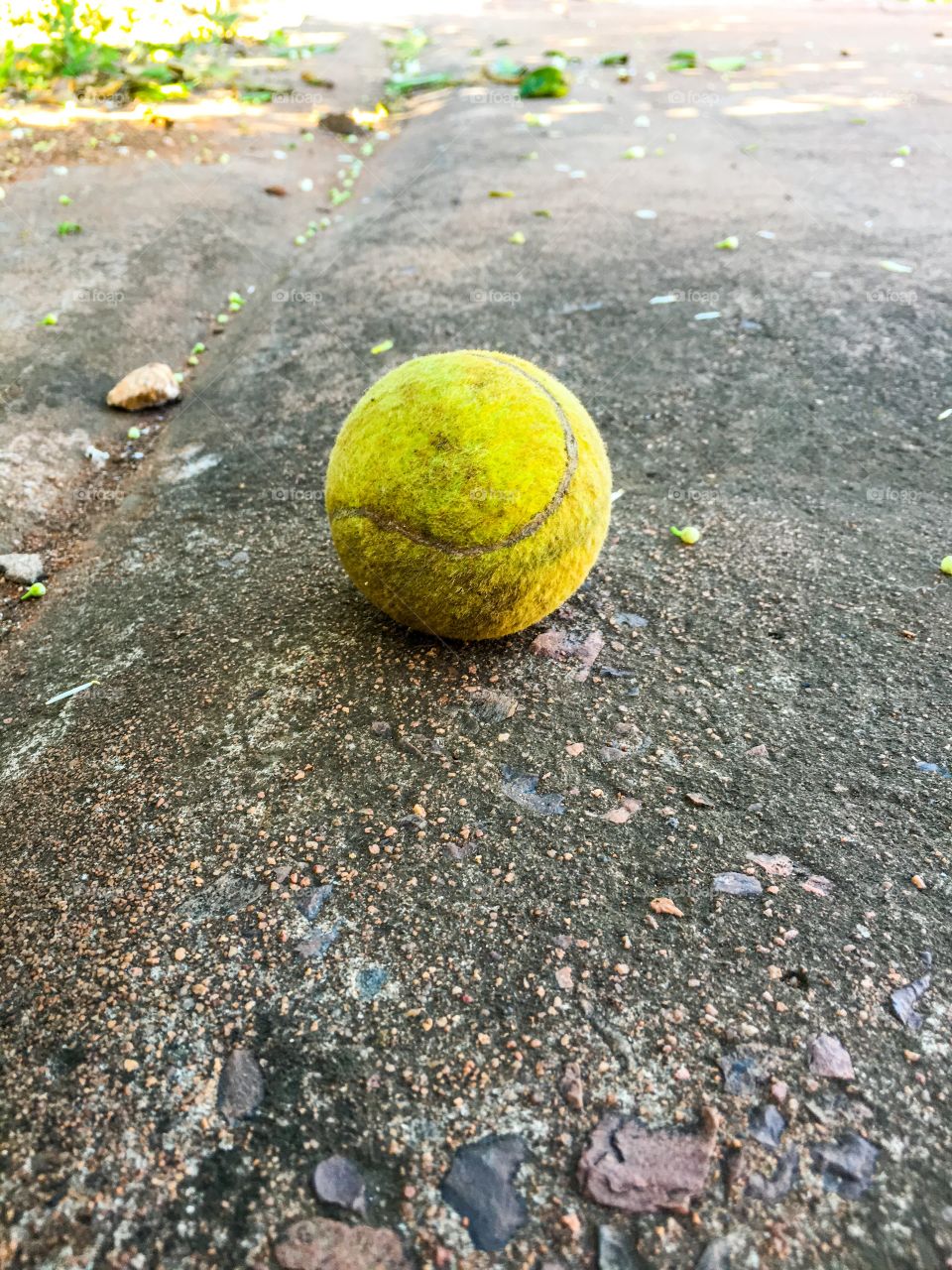 Dirty old tennis ball closeup perspective on dirty sidewalk path