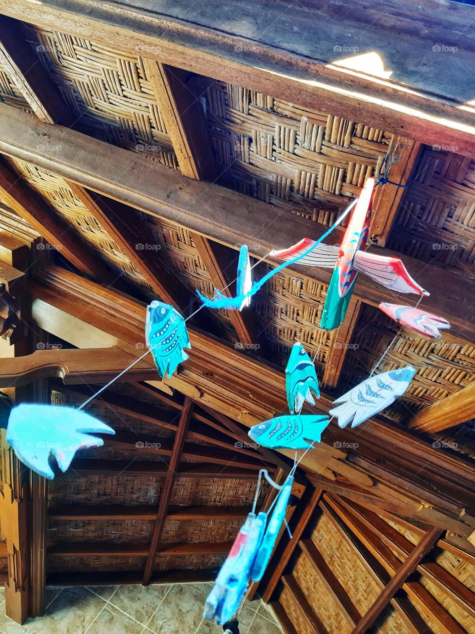 The fish-shaped colorful toy which is hanged on the brown wooden ceilings