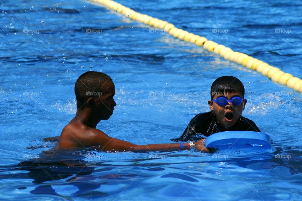 young kid learns how to swim with the help of a swimming coach