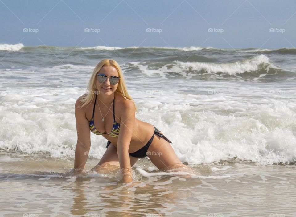 The girl is sitting on the shore in the sea with waves and white foam.