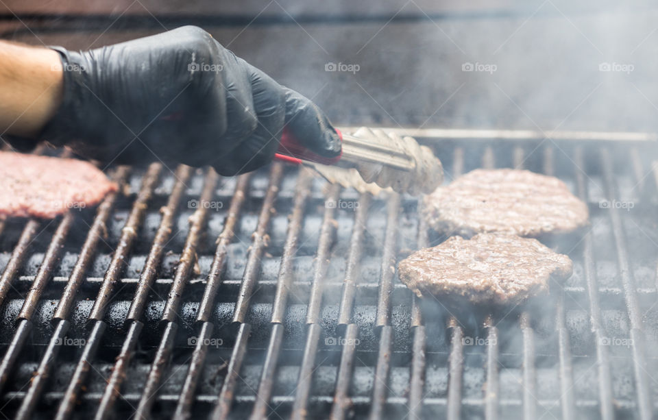 Cook's hand in glove fries meat burgers cutlets on a steaming grill. Outdoor barbeque cooking.