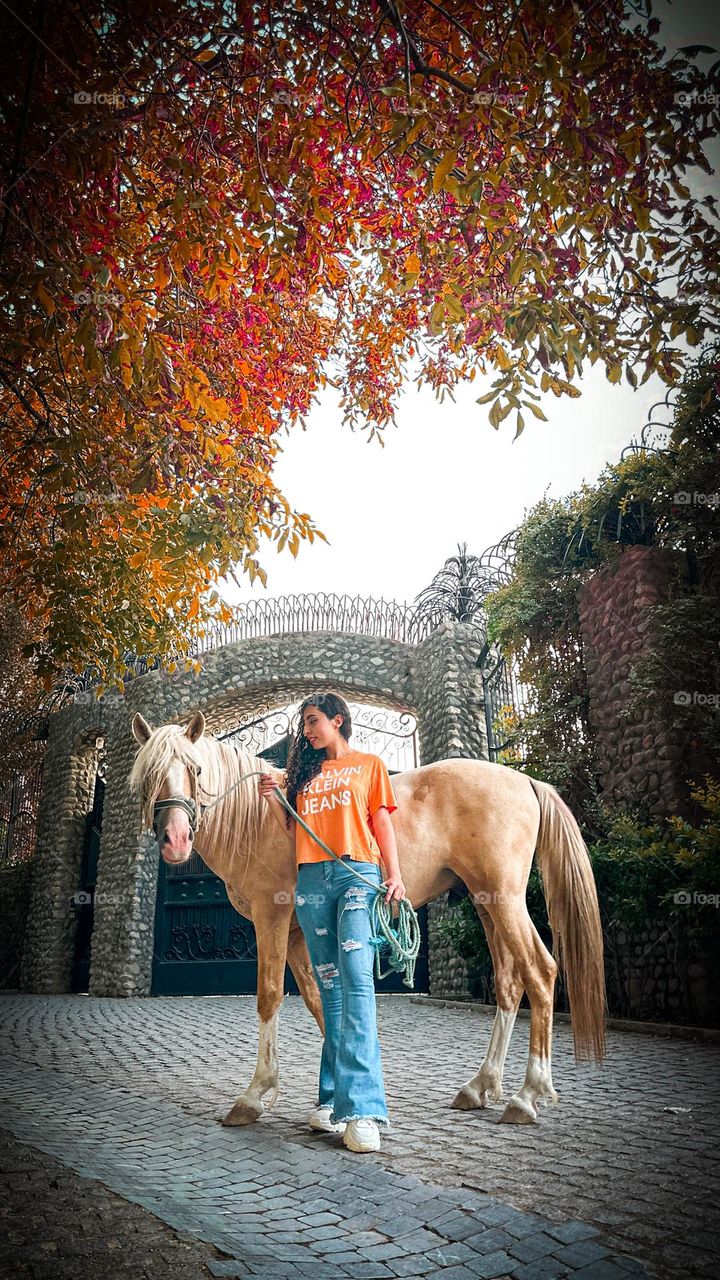 A girl with curly hair next to a horse in an autumn mood