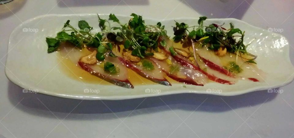Fish sashimi with sauce and green sprouts on a fancy plate