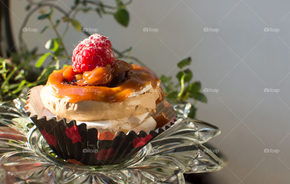 Decadent caramel cupcake with chocolate and fresh raspberry garnish sprinkled with powdered sugar dust in golden hour sun : dreamy summertime dessert background with room for copy
