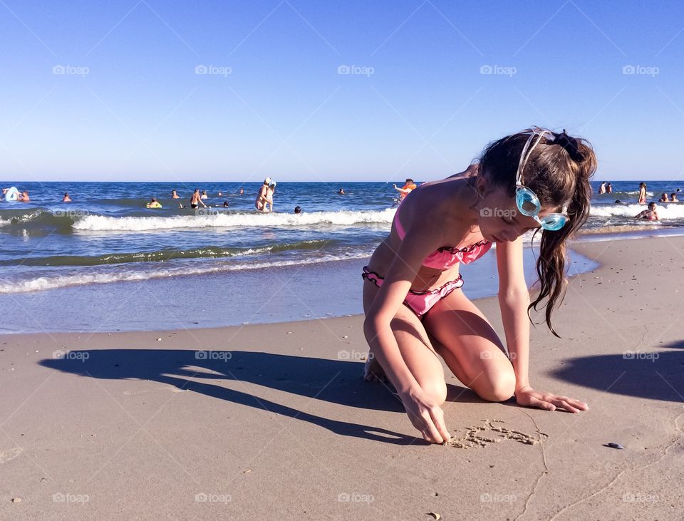 Girl on a beach writing on a sand 