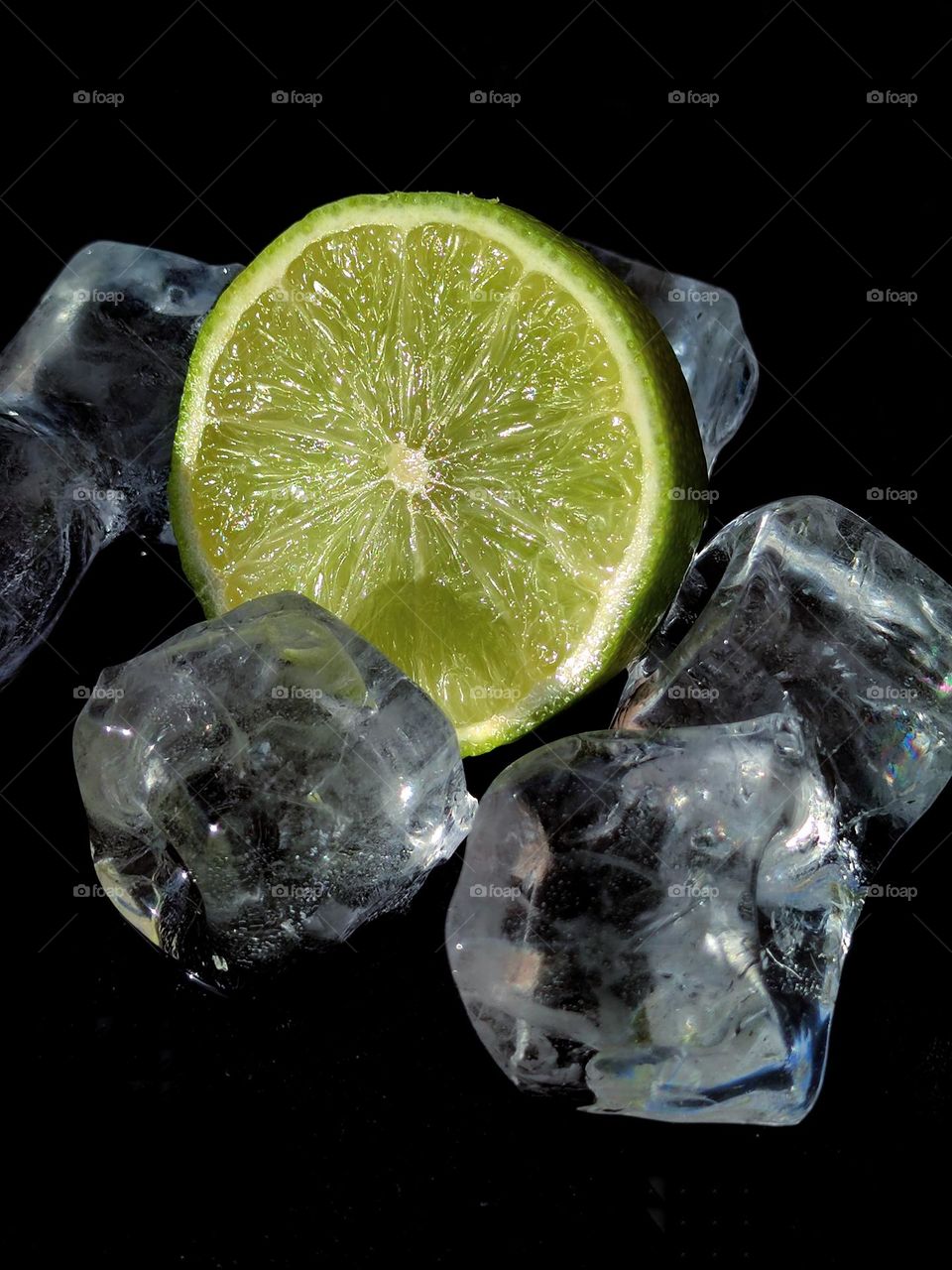 Juicy lime.  Half of a green lime among pieces of ice on a black background