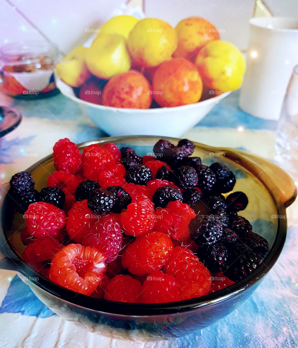 Appetizing berries. On the table is a plate with raspberries and blackberries.