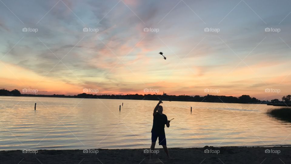 Beautiful sunset photo of young man silhouetted by the lighting and performing with his flower sticks! 
