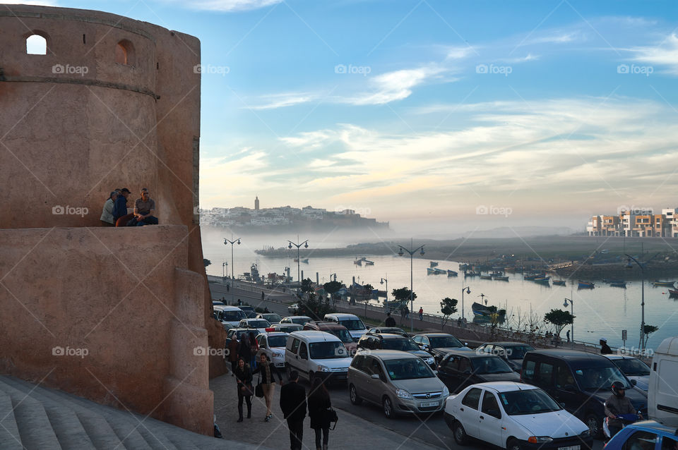 View from the street filled with cars (Rabat, Morocco) at the mouth of the Bou Regrer river under a cloudy sky lit by the setting sun on a spring evening