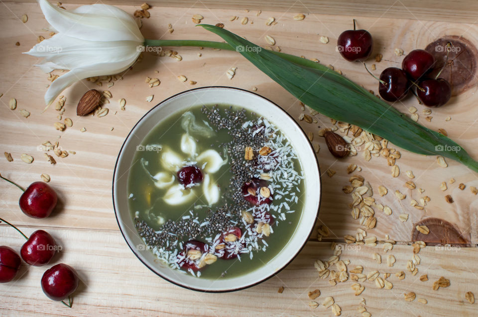 Beautiful smoothie bowl background photography of artisanal food  design with fresh dark red cherries, coconut, almond, chia, protein powder and mango in green smoothie bowl with white flower design 
