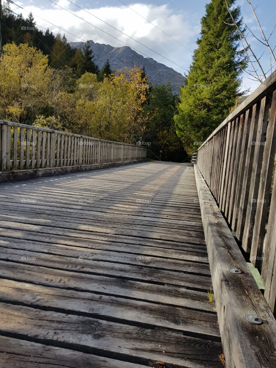 Verwitterte alte Holzbrücke über die Isar, im Hintergrund herbstliche Bäume und Berge