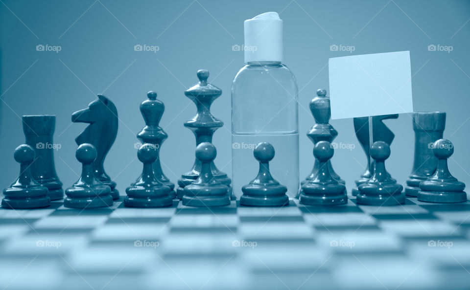 Coronavirus concept image chess pieces and hand sanitizer on chessboard illustrating global struggle against novel covid-19 outbreak.