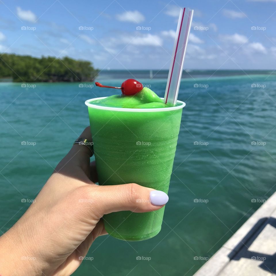 A fruity green cocktail with a cherry on top overlooking the blue water of the Caribbean Sea