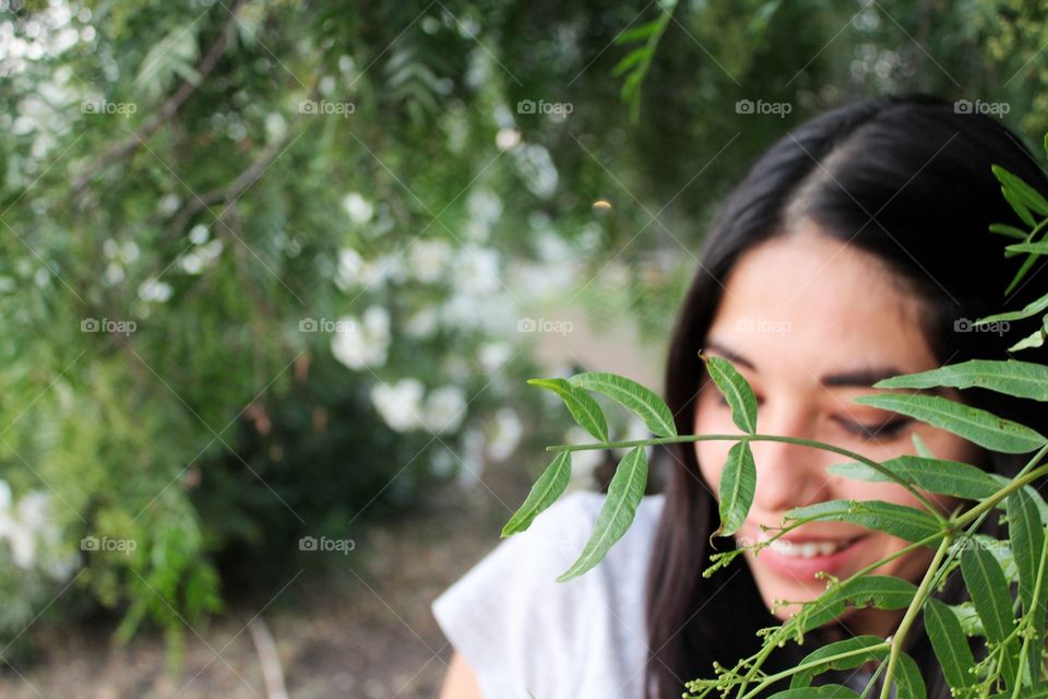 Portrait of beautiful young woman standing among green shrubs and a pepper tree. 
