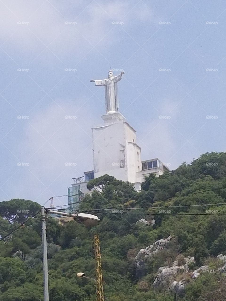 In 1950, Abouna Yaacoub purchased the hill located to the right of Nahr el-Kalb river, and started the construction of the convent and the church. On December 1, 1952, the hill was crowned by a statue of Christ the King, with a height of 12 meters, the width of its open hands reached 10 meters, and it weighed 75 tons, which was designed by the Italian artist Ernesto Pallini. Thus, the old dream came true after about fifty-eight years!

The statue of Christ the King is now erected on the hill called “The Ruins of Kings” in Zouk Mosbeh, Keserwan district, Mount Lebanon Governorate. Jesus refers with his right hand to Virgin Mary, in the temple of Our Lady of Lebanon, and with his left hand to the righteous educator, in the convent of Saint Joseph of The Tower, as if he is reuniting the Nazareth family here again! While all those kings and greats whose names are carved on those rocks are lost in the unseen and oblivion! They are all gone, and Jesus is staying as is, yesterday, today and forever.