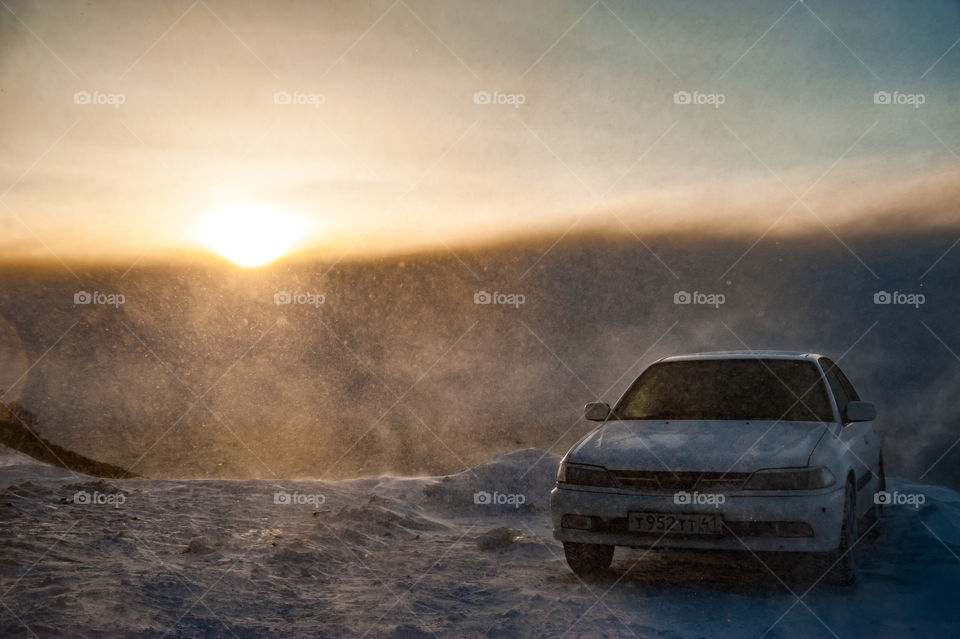 during a blizzard, a car stands on the edge of a mountain, the sun is visible through the clouds
