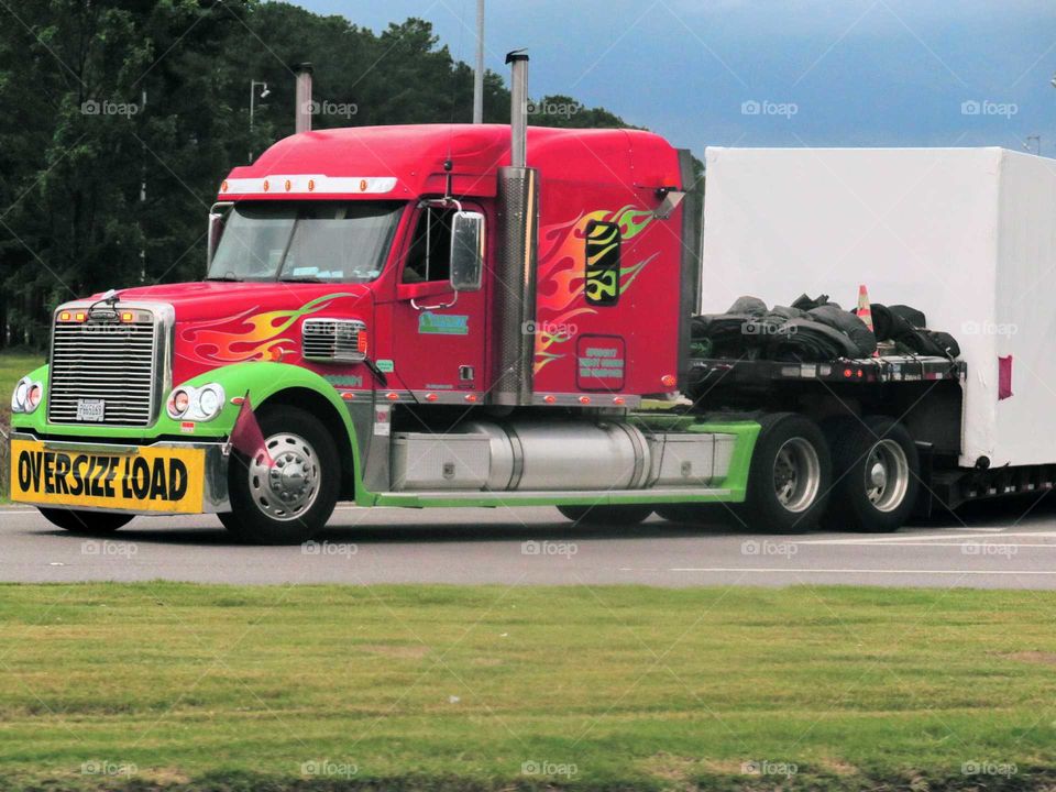 A red and green 18 wheeler pulling an oversized load.