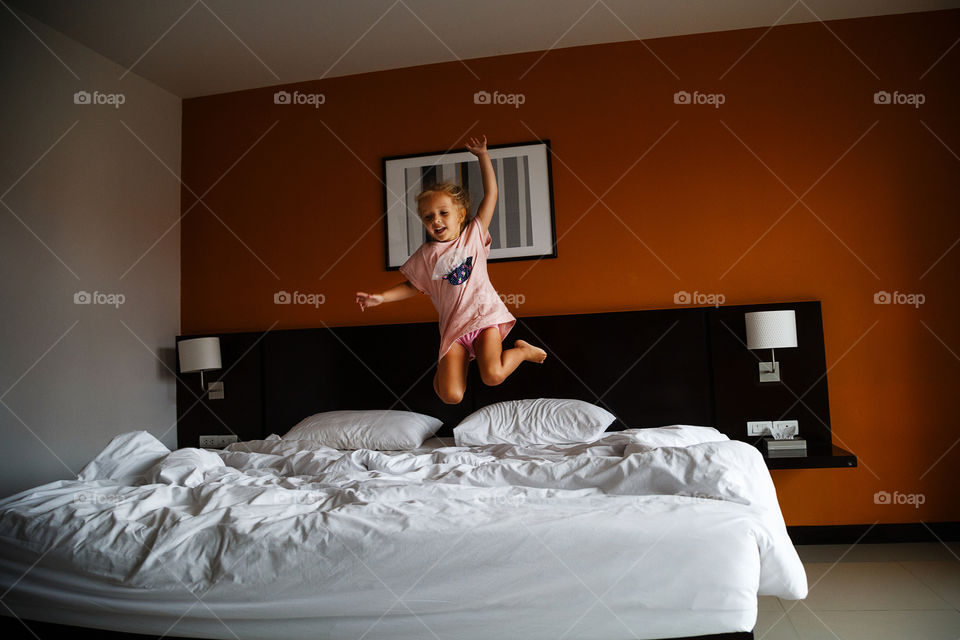 Happy little girl with blonde hair jumping on the bed