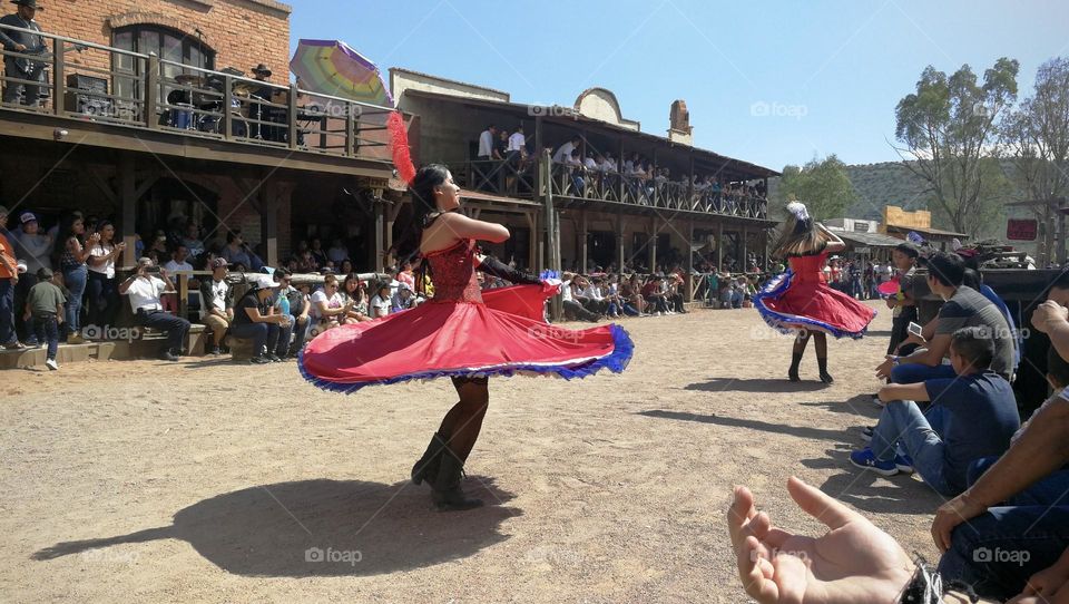 Women dressed with red skirts, dancing on rustic street.