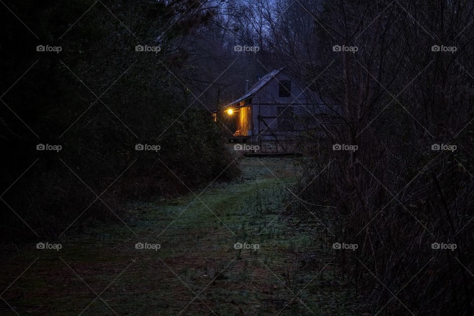 An old country house at a distance during twilight hours with a warm inviting glow from the front porch light. Belvidere Tennessee. 