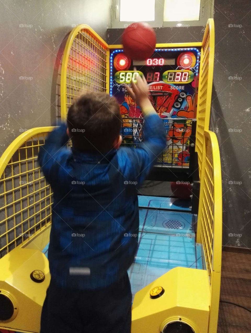 child playing payed basketball game machine, colourful