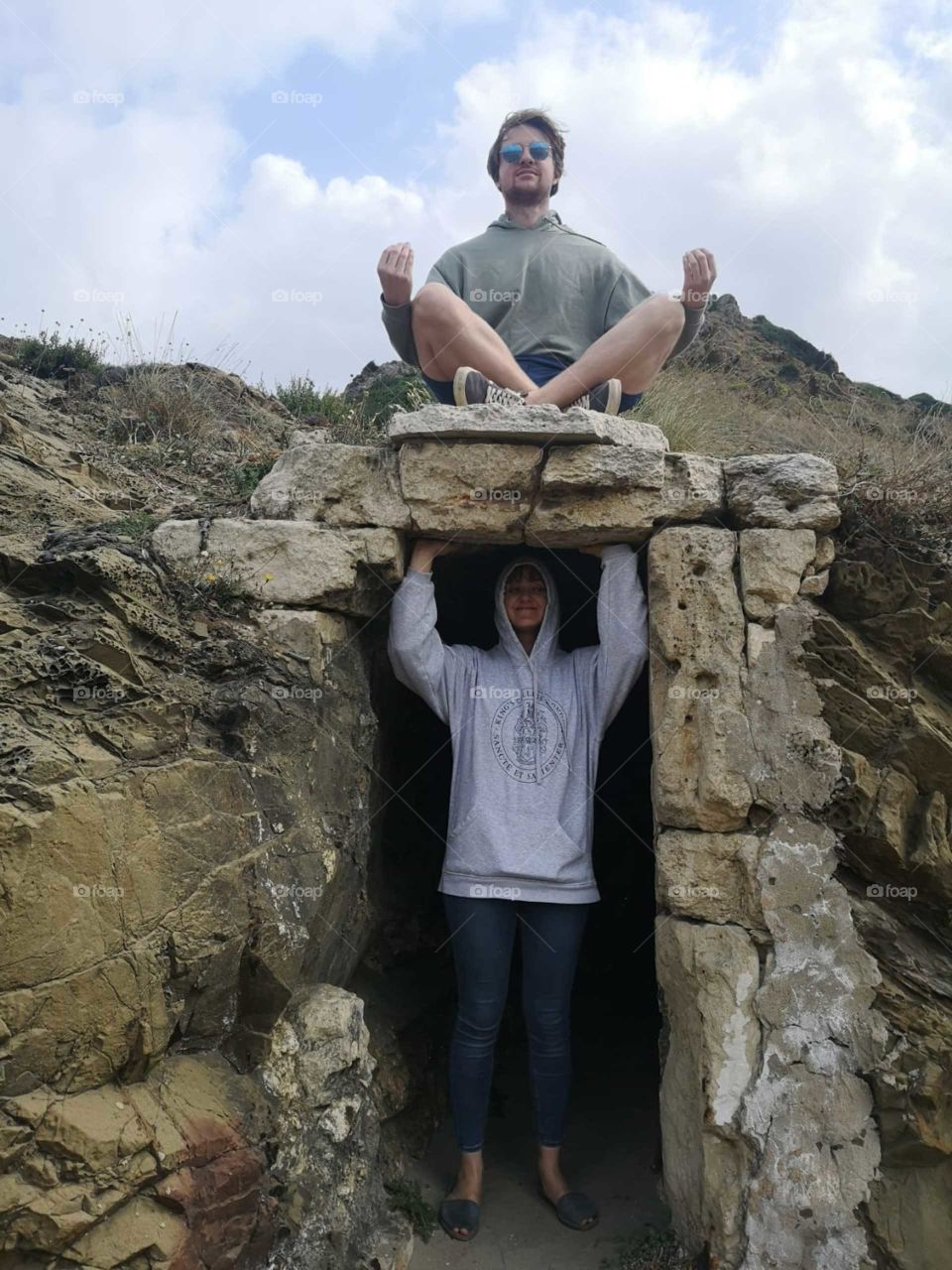 Two people, rock? Playing. One is in a man made cavern, pretending to hold up rock that the other is meditating on
