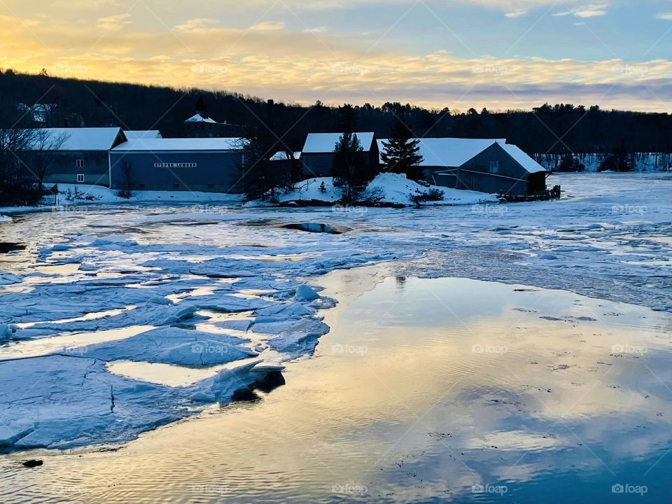 A sunrise over an icy river reflects the pastel sky.