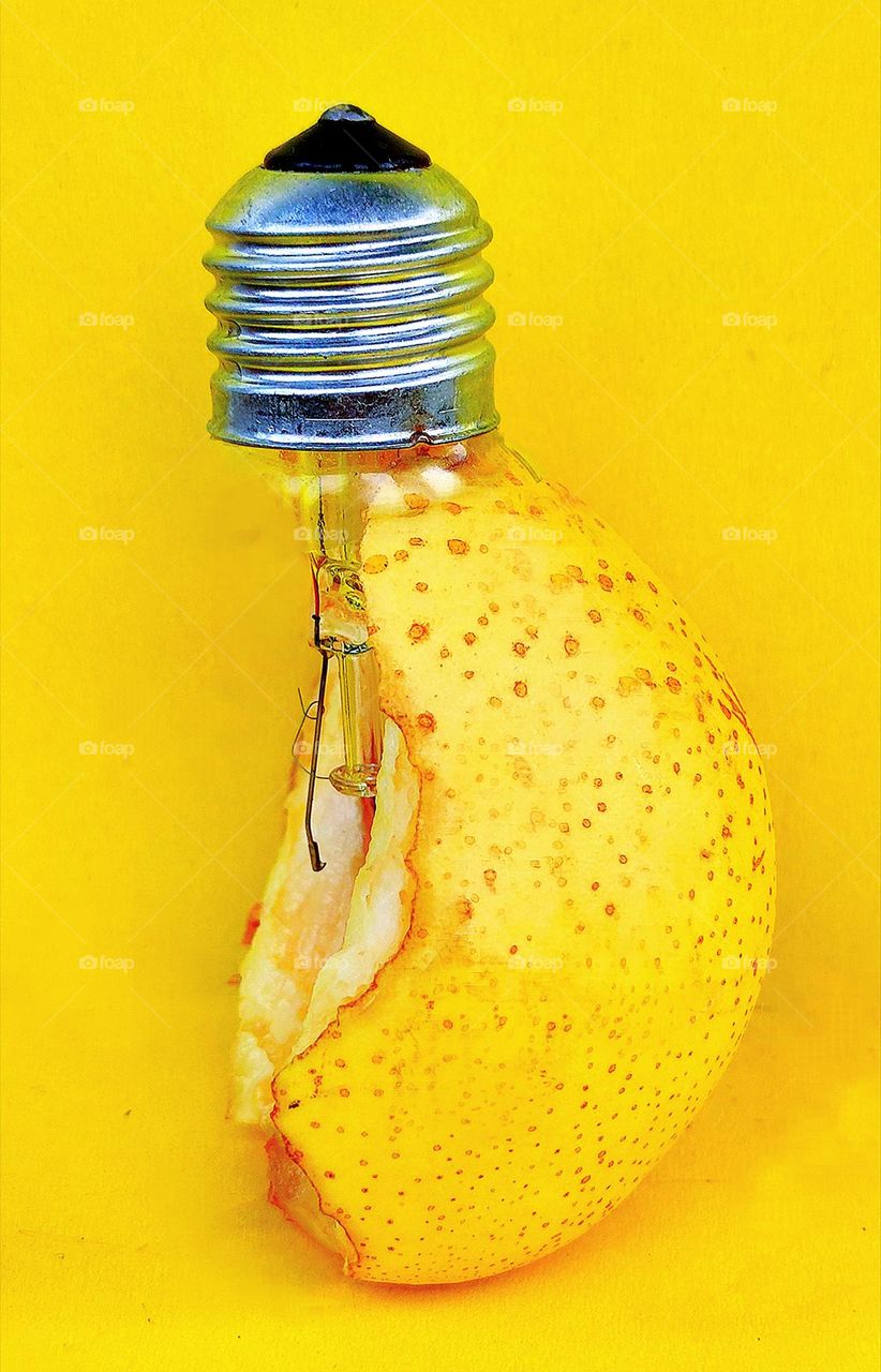 On a yellow background, a combination of a light bulb (metal base and metal electrode filaments) and a yellow pear.  Photo metaphor.  A pear looks like a light bulb