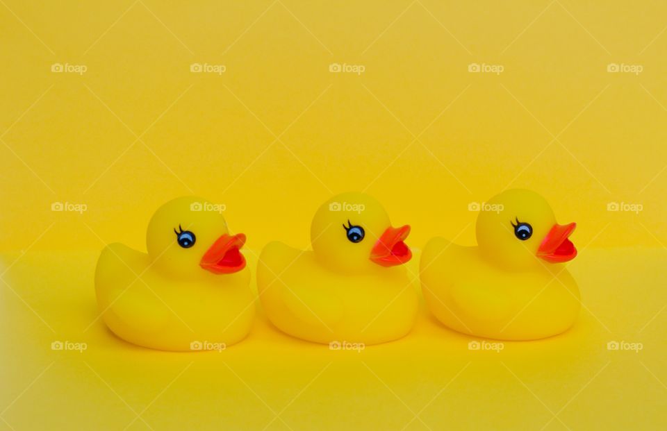 Three yellow rubber ducks in a row on a yellow background 