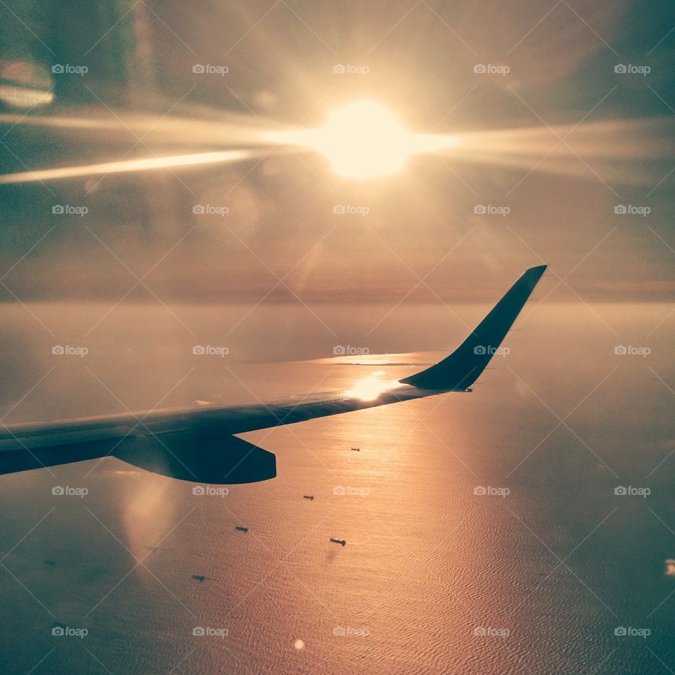 airplane wing upon descent. sunset sparkles on the ocean from the plane
