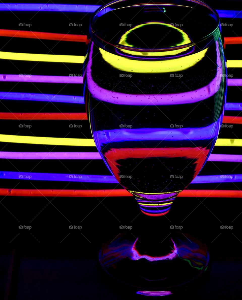 Abstract colorful glow sticks reflecting into a glass of water with a black background 