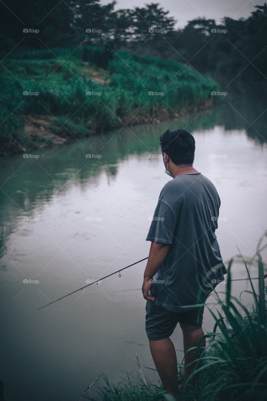A man wearing a grey shirt is fishing in the river