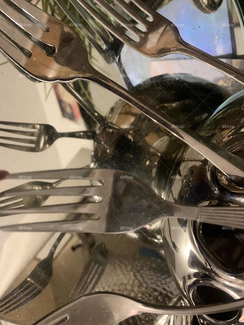 Forks sticking out of vase sitting on top of a mirror 