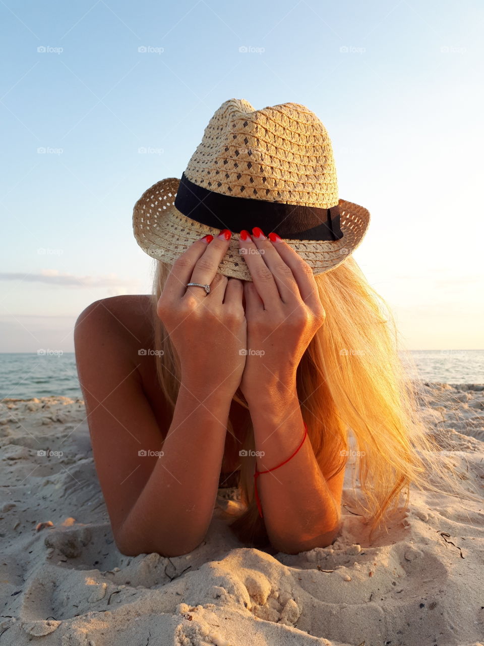 Blonde girl with hat lying on the sand