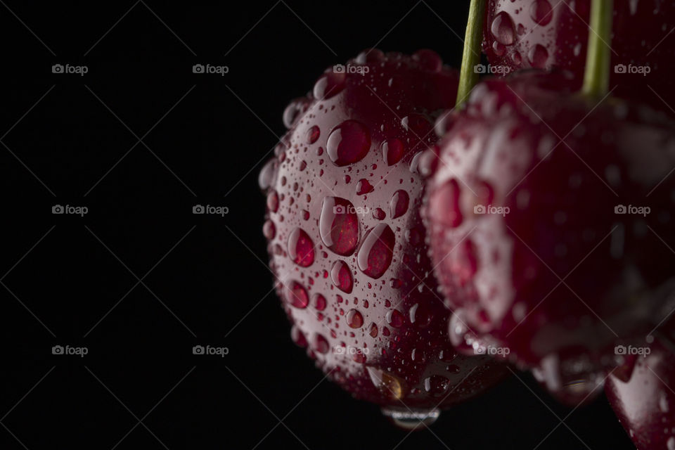 macro shot of red ripe cherry covered with rain drops on black background